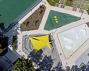 Campus Efeuweg, Berlin Neukölln Foto des Forum am Campus Efeuweg, einer multifunktionalen, modernen Landschaftsarchitektur mit Amphitheater, Sportfeld, Gemeinschaftsgarten und Bewegungsflächen. Der Platz ist umgeben von Grünflächen, bietet barrierefreien Zugang und dient als Treffpunkt für Schüler, Nachbarschaft und Veranstaltungen. Das Amphitheater ist mit Sonnensegeln ausgestattet, die Bewegungsflächen sind leicht modelliert, und das gesamte Areal verbindet den Schulhof mit dem öffentlichen Raum in einem urbanen Design.